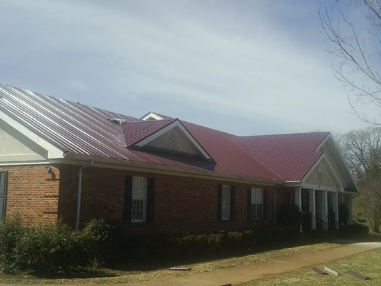 Red metal roof with gabled entries on a long brick building, from a Hail Damage Roof Repair job in Yarnell