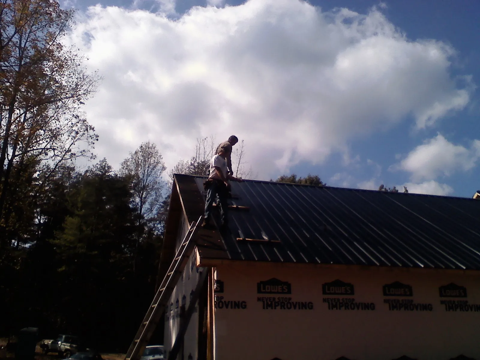Roofer fastening dark metal panels high against a cloudy sky, from a Roof Inspection job in Yarnell